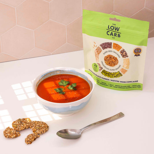 Cracked black pepper from The Low Carb Co displayed in a clear jar with a wooden lid on a rustic wooden background.